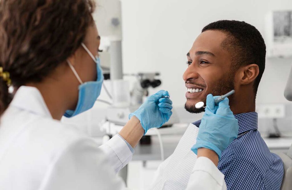 Person brushing their tongue beside a bathroom sink with a toothbrush, floss, and glass of water nearby.